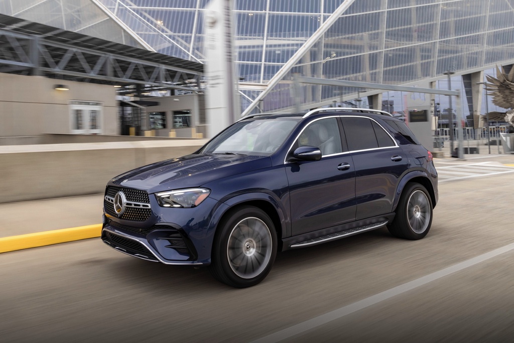 Dark blue Mercedes-Benz SUV driving on urban roadway near modern glass building