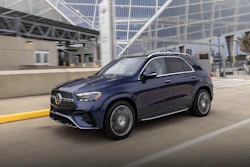 Dark blue Mercedes-Benz SUV driving on urban roadway near modern glass building