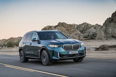 Blue BMW X-series SUV driving on mountain road at sunset