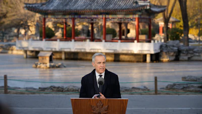 Government official speaking at podium near traditional Chinese pavilion in autumn