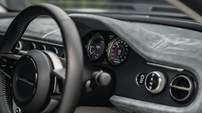 Close-up of car dashboard with analog speedometer and carbon fiber trim