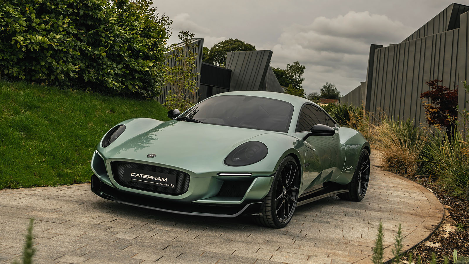 Green Caterham sports car parked on stone driveway with garden background