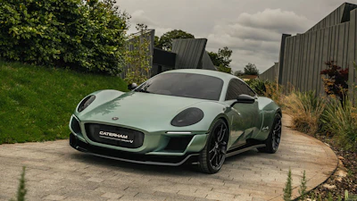 Green Caterham sports car parked on stone driveway with garden background