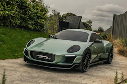 Green Caterham sports car parked on stone driveway with garden background