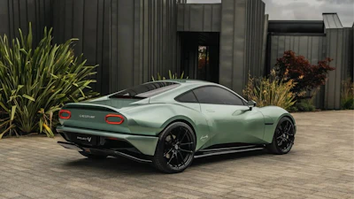 Sage green Aston Martin sports car parked on brick pavement with modern building background