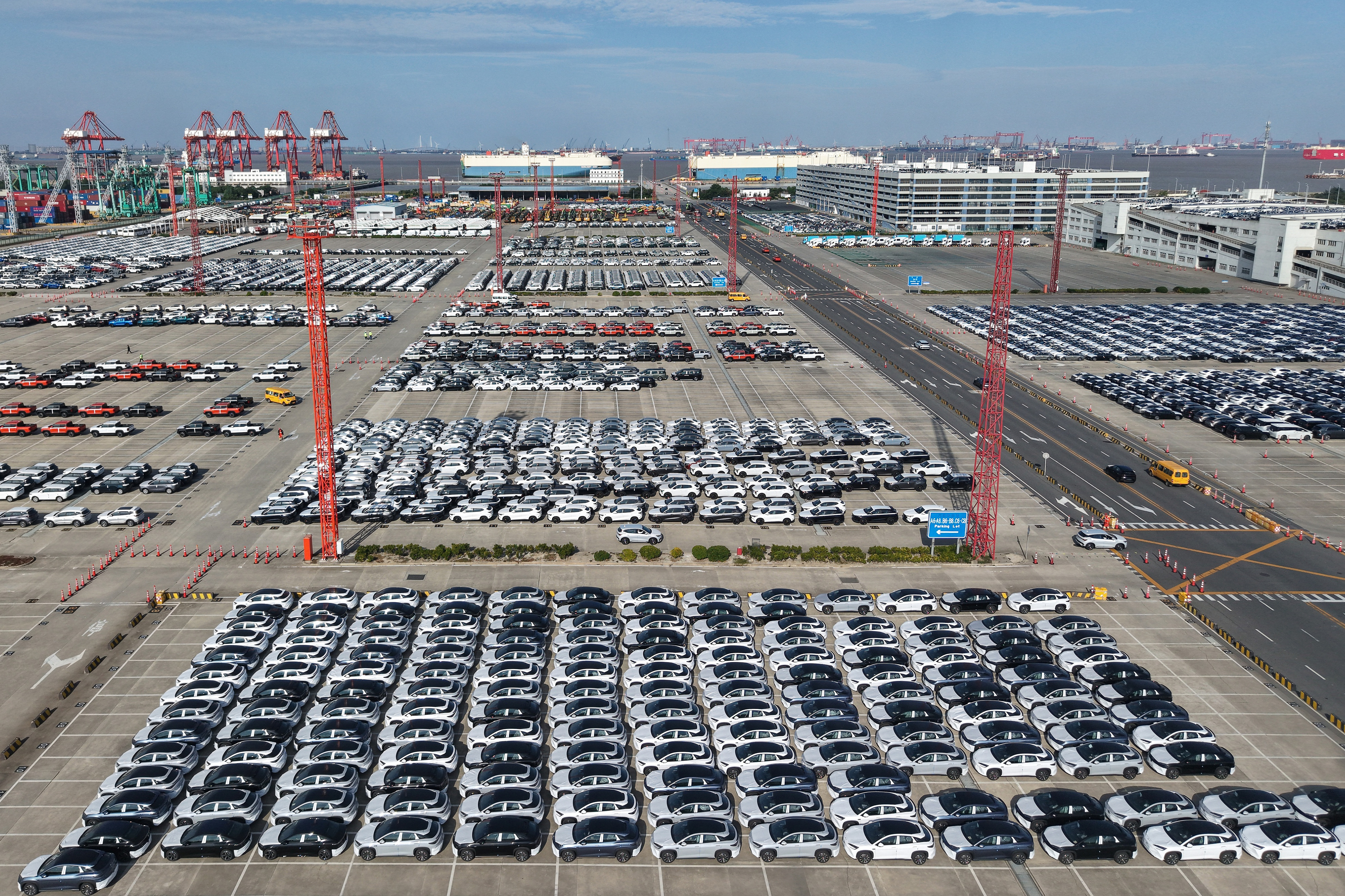 Aerial view of massive car storage lot with hundreds of vehicles near shipping cranes