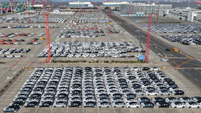 Aerial view of massive car storage lot with hundreds of vehicles near shipping cranes