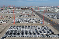 Aerial view of massive car storage lot with hundreds of vehicles near shipping cranes
