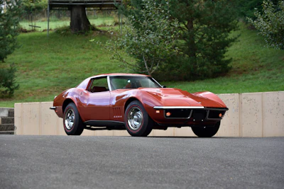 Classic red 1970s Corvette Stingray parked on asphalt with green trees in background