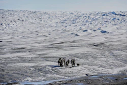Small group of people walking across a vast, icy Arctic or Antarctic landscape