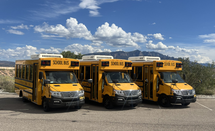 Three yellow school buses parked in a desert landscape with mountains and cloudy sky