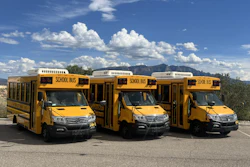 Three yellow school buses parked in a desert landscape with mountains and cloudy sky