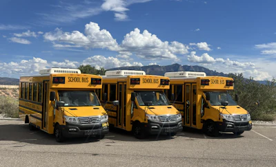 Three yellow school buses parked in a desert landscape with mountains and cloudy sky