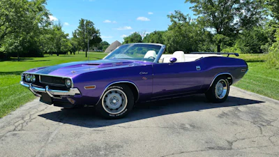 Classic purple Dodge Challenger convertible parked on concrete with green trees in background