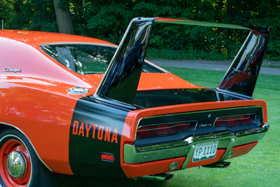 Classic orange Dodge Daytona muscle car with open wing, parked on grass