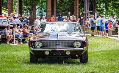 Classic burgundy muscle car displayed on grass at outdoor car show