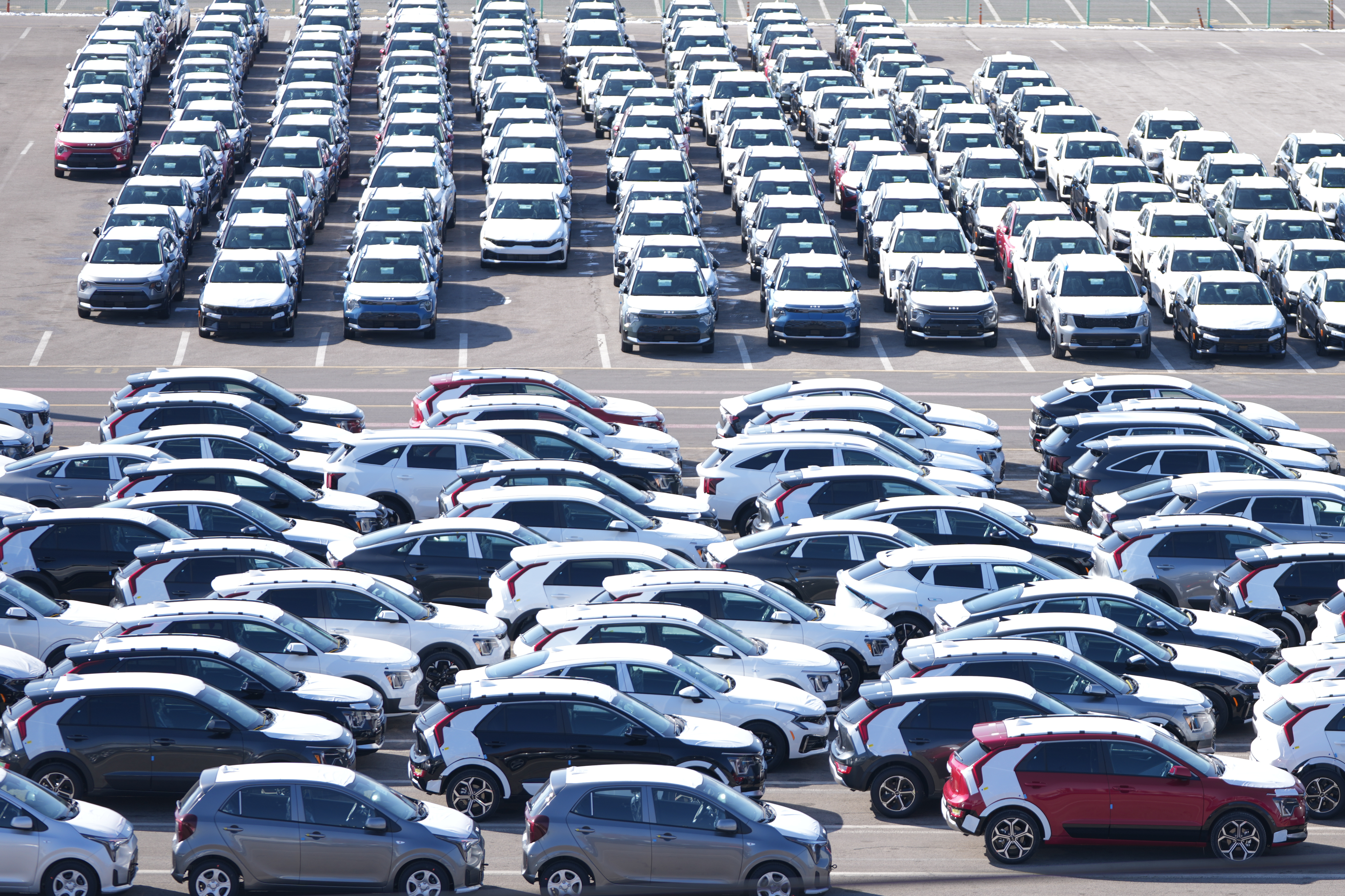 Aerial view of parking lot with rows of white, gray, and black vehicles