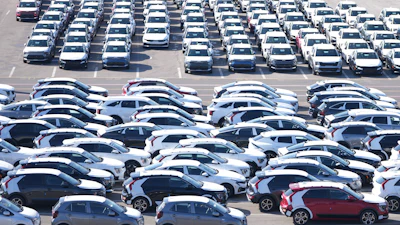 Aerial view of parking lot with rows of white, gray, and black vehicles