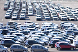 Aerial view of parking lot with rows of white, gray, and black vehicles
