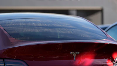 Red Tesla electric vehicle with company logo, parked near Tesla signage