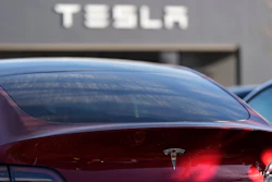 Red Tesla electric vehicle with company logo, parked near Tesla signage