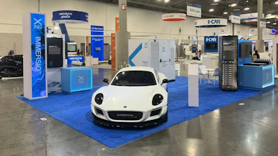 White sports car displayed on blue floor at technology trade show booth