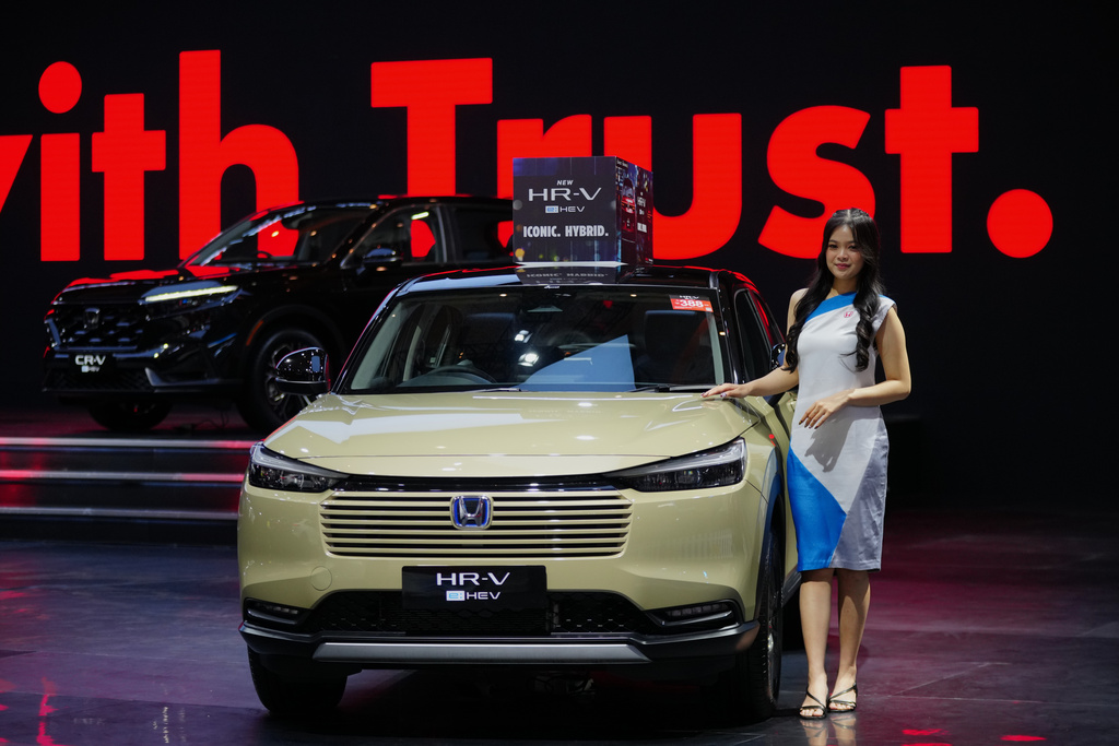 Honda HR-V hybrid SUV in pale yellow, displayed at automotive event with red backdrop