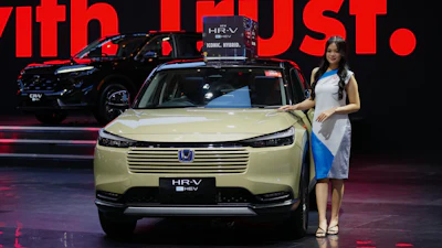 Honda HR-V hybrid SUV in pale yellow, displayed at automotive event with red backdrop