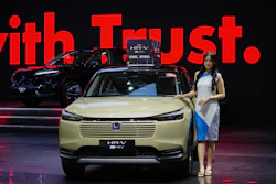 Honda HR-V hybrid SUV in pale yellow, displayed at automotive event with red backdrop
