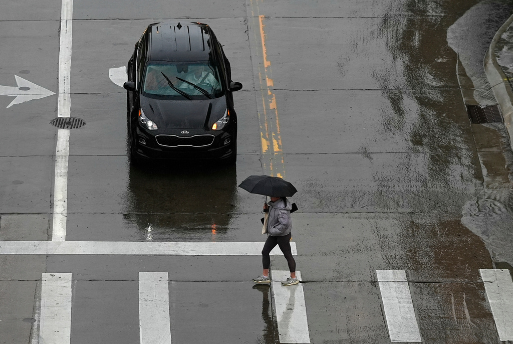 Black Kia car stopped at crosswalk during rainy day, pedestrian with umbrella crossing street
