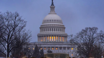 U.S. Capitol Building illuminated at dusk with bare winter trees and classical dome architecture