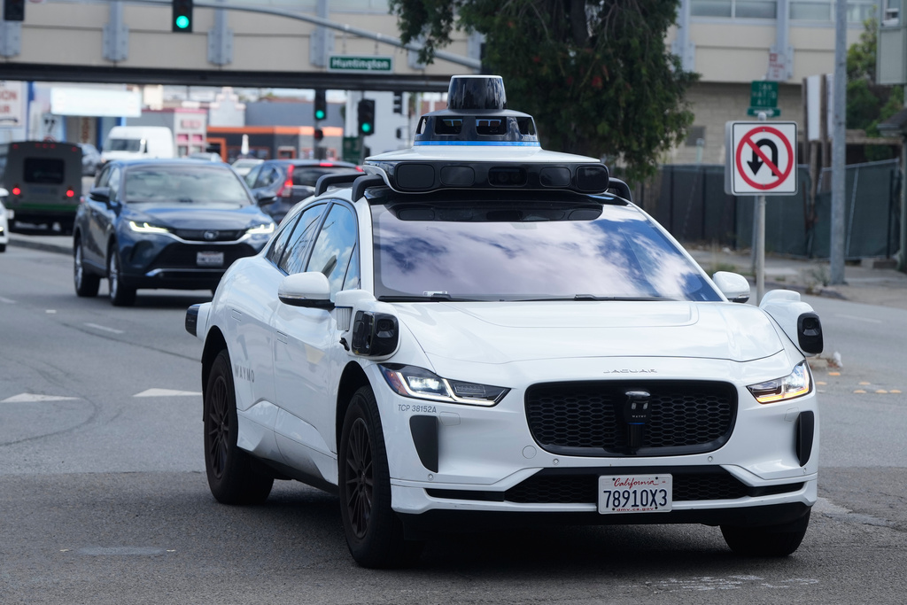 White Waymo autonomous vehicle with blue roof sensors driving on urban street among traffic