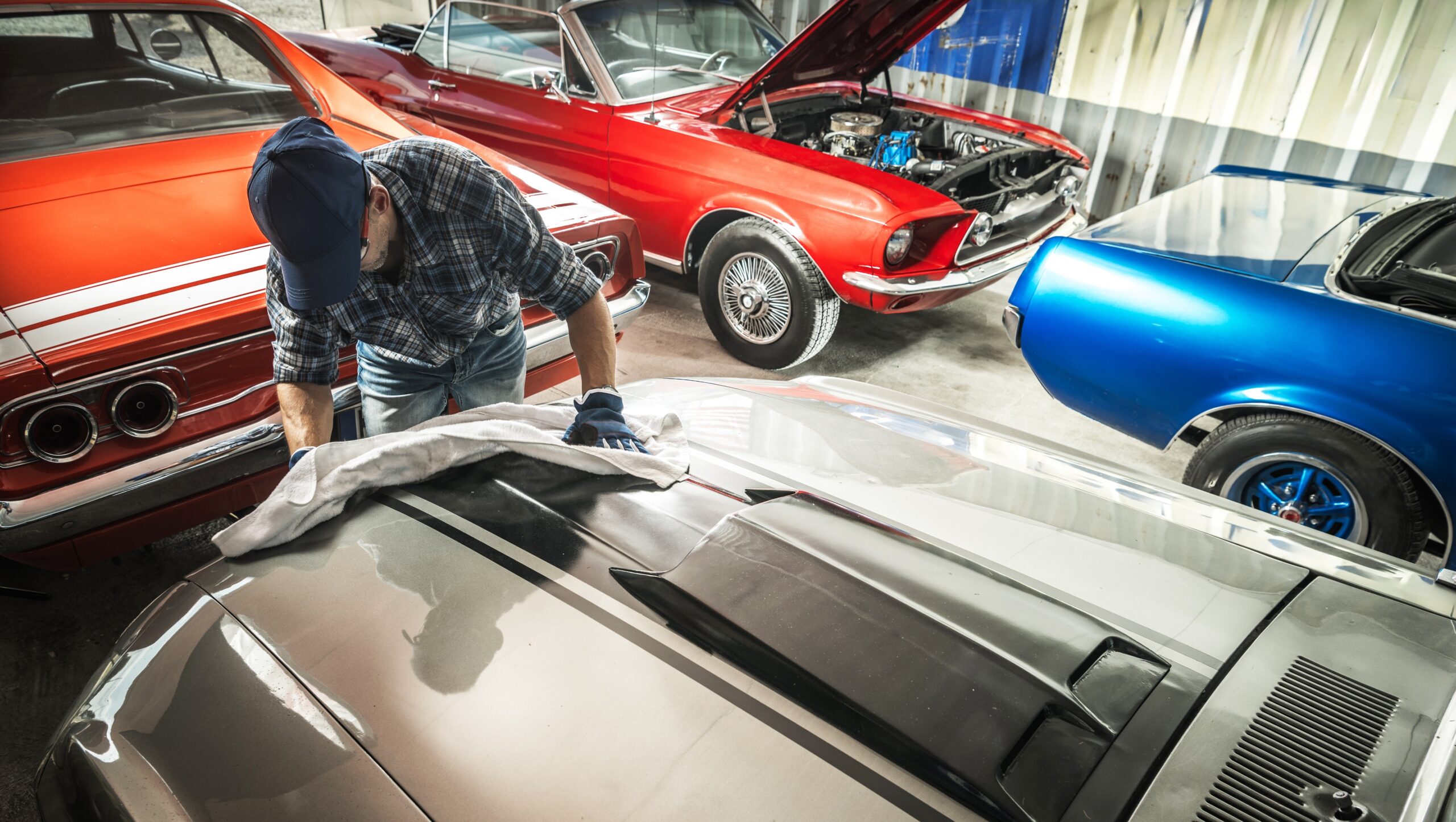 Classic muscle cars in workshop with mechanic working on silver vehicle