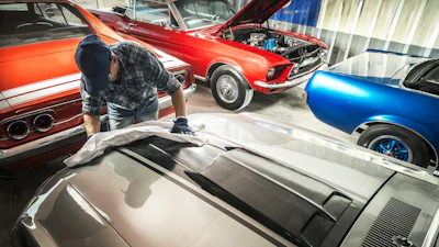 Classic muscle cars in workshop with mechanic working on silver vehicle