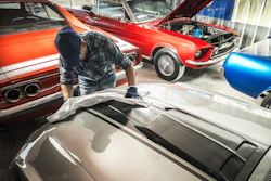 Classic muscle cars in workshop with mechanic working on silver vehicle