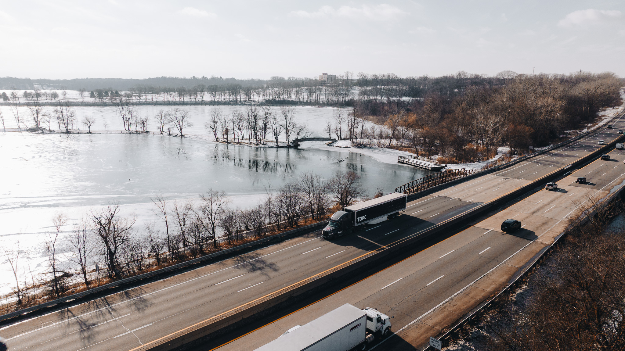 Aerial view of highway bridge spanning frozen river with bare trees and winter landscape