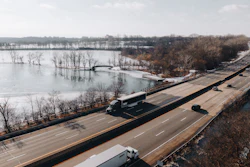 Aerial view of highway bridge spanning frozen river with bare trees and winter landscape