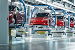 Red Tesla vehicles on automated assembly line in modern manufacturing facility with blue robotic equipment