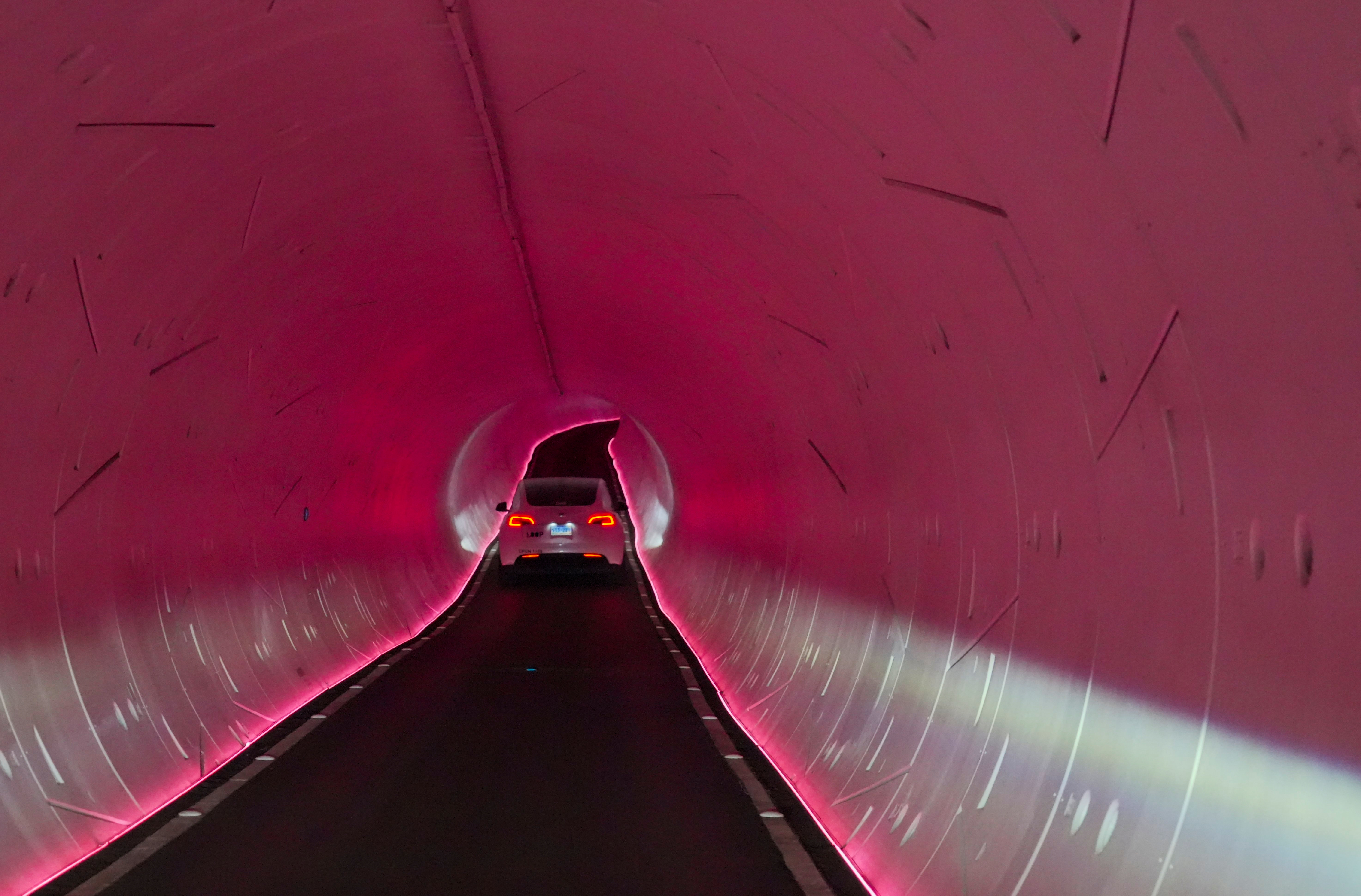 Car driving through illuminated pink tunnel with curved walls