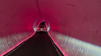 Car driving through illuminated pink tunnel with curved walls