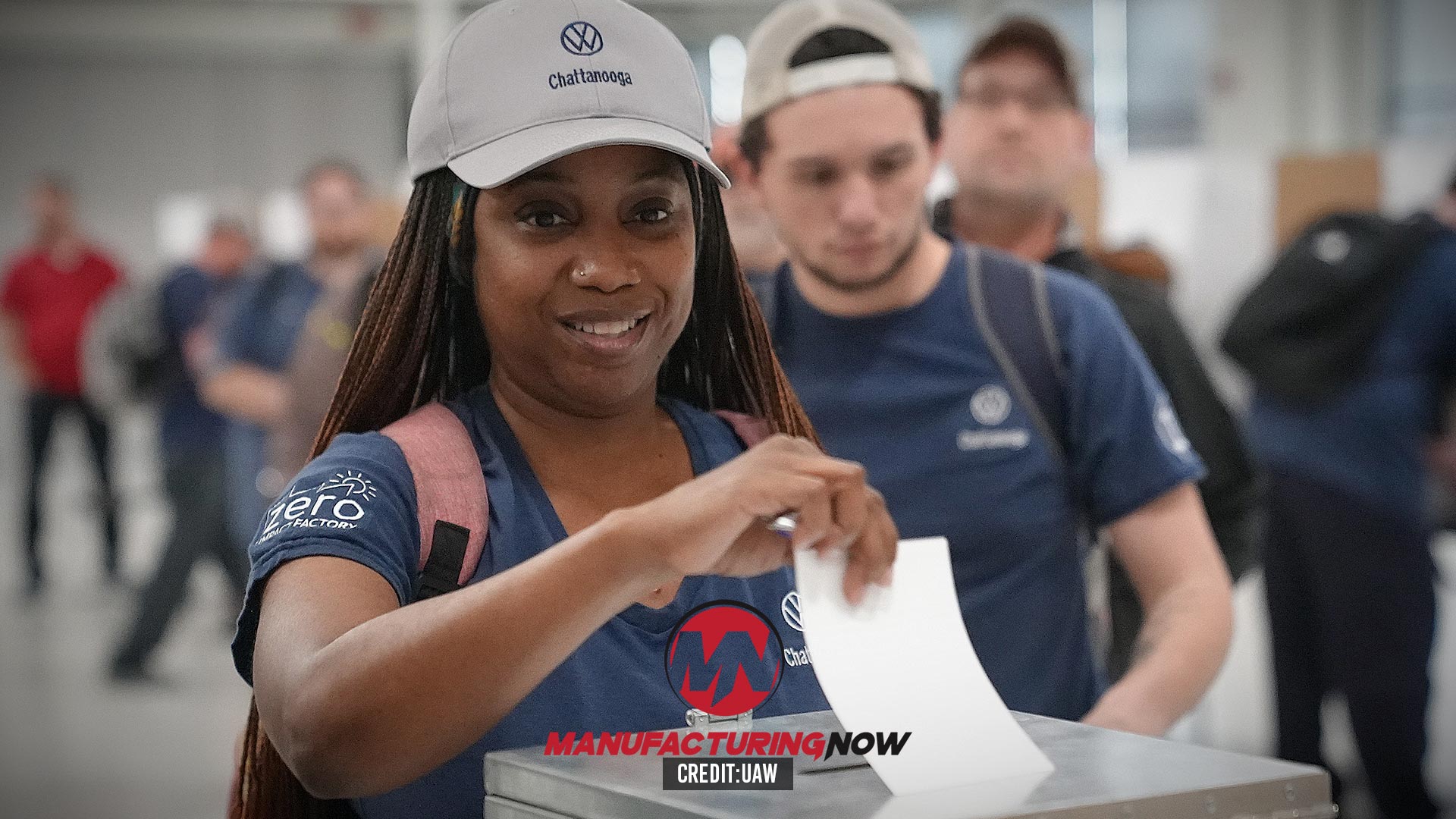 Smiling woman in Volkswagen cap and Manufacturing Now shirt at corporate event with colleagues