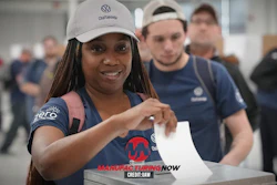Smiling woman in Volkswagen cap and Manufacturing Now shirt at corporate event with colleagues
