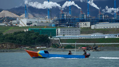 Colorful fishing boat near industrial plant with smoking chimneys on coastal landscape