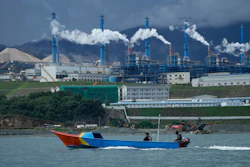 Colorful fishing boat near industrial plant with smoking chimneys on coastal landscape