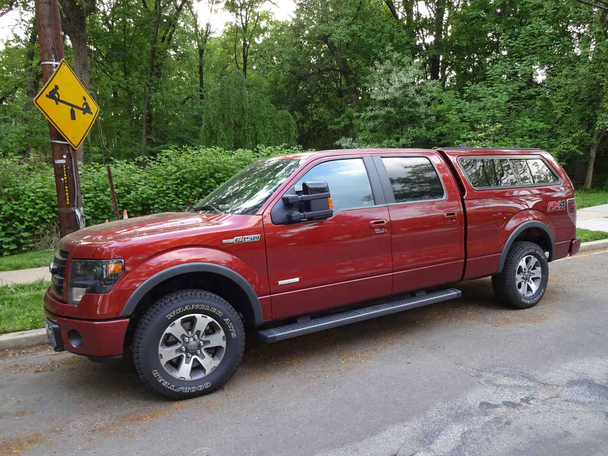 Deep red Ford F-150 pickup truck parked on residential street with trees in background