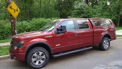 Deep red Ford F-150 pickup truck parked on residential street with trees in background