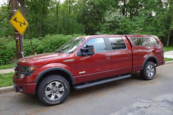 Deep red Ford F-150 pickup truck parked on residential street with trees in background