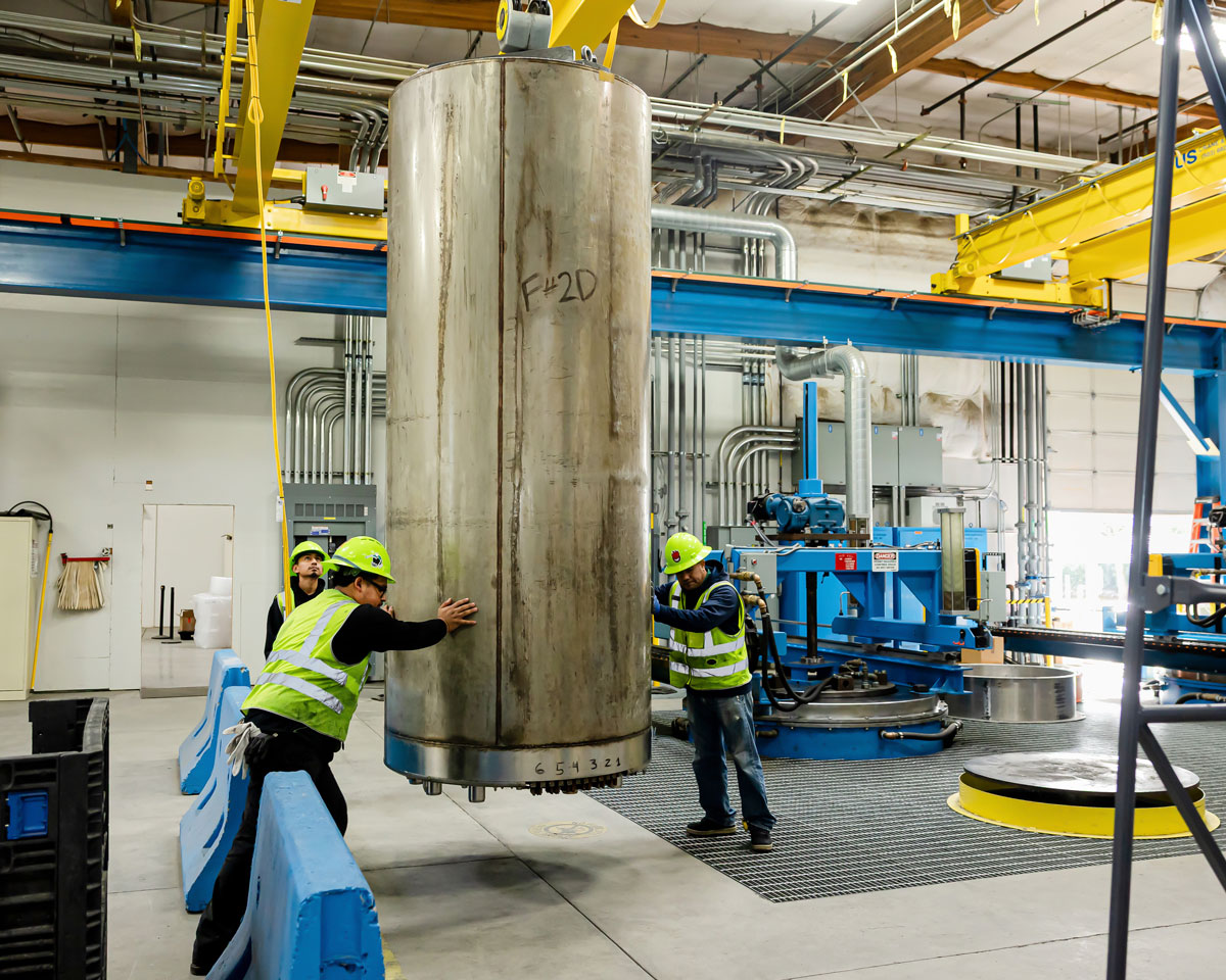 Industrial workers in safety gear inspect large metal cylinder in manufacturing facility