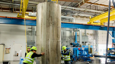 Industrial workers in safety gear inspect large metal cylinder in manufacturing facility