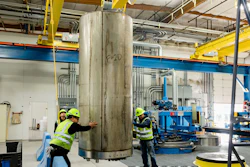 Industrial workers in safety gear inspect large metal cylinder in manufacturing facility